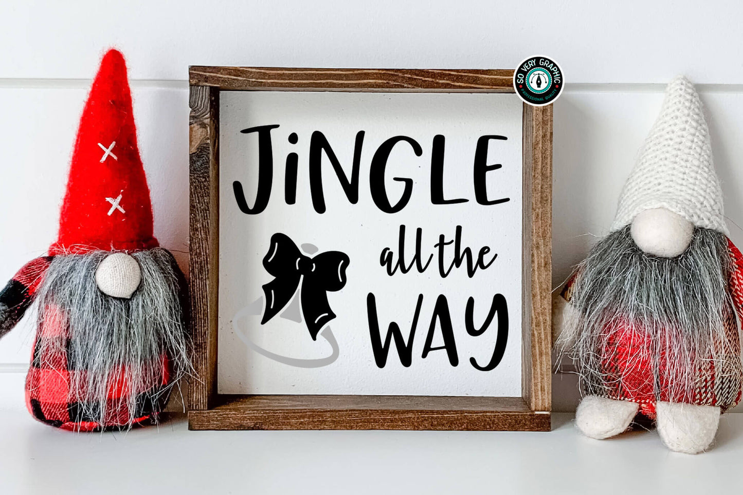 Jingle All the Way SVG Design in a rustic wood frame sitting on a counter between two holiday gnomes wearing Buffalo plaid