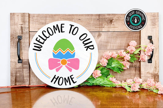 Welcome to Our Home SVG design on a white wood round in a spring farmhouse scene.