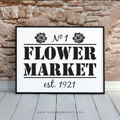 Flower Market Sign in a black frame sitting on the hardwood floors with an exposed stone wall behind the frame