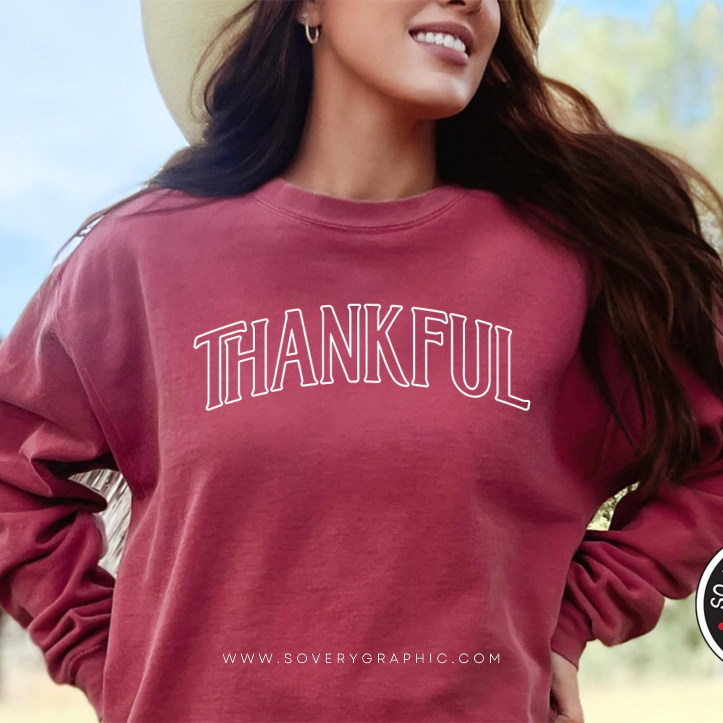 Woman wearing a maroon sweatshirt with 'THANKFUL' text, outdoors.