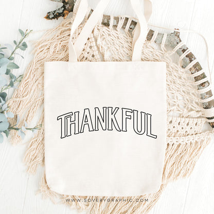 White tote bag with 'THANKFUL' text on a decorative background with macrame and greenery.