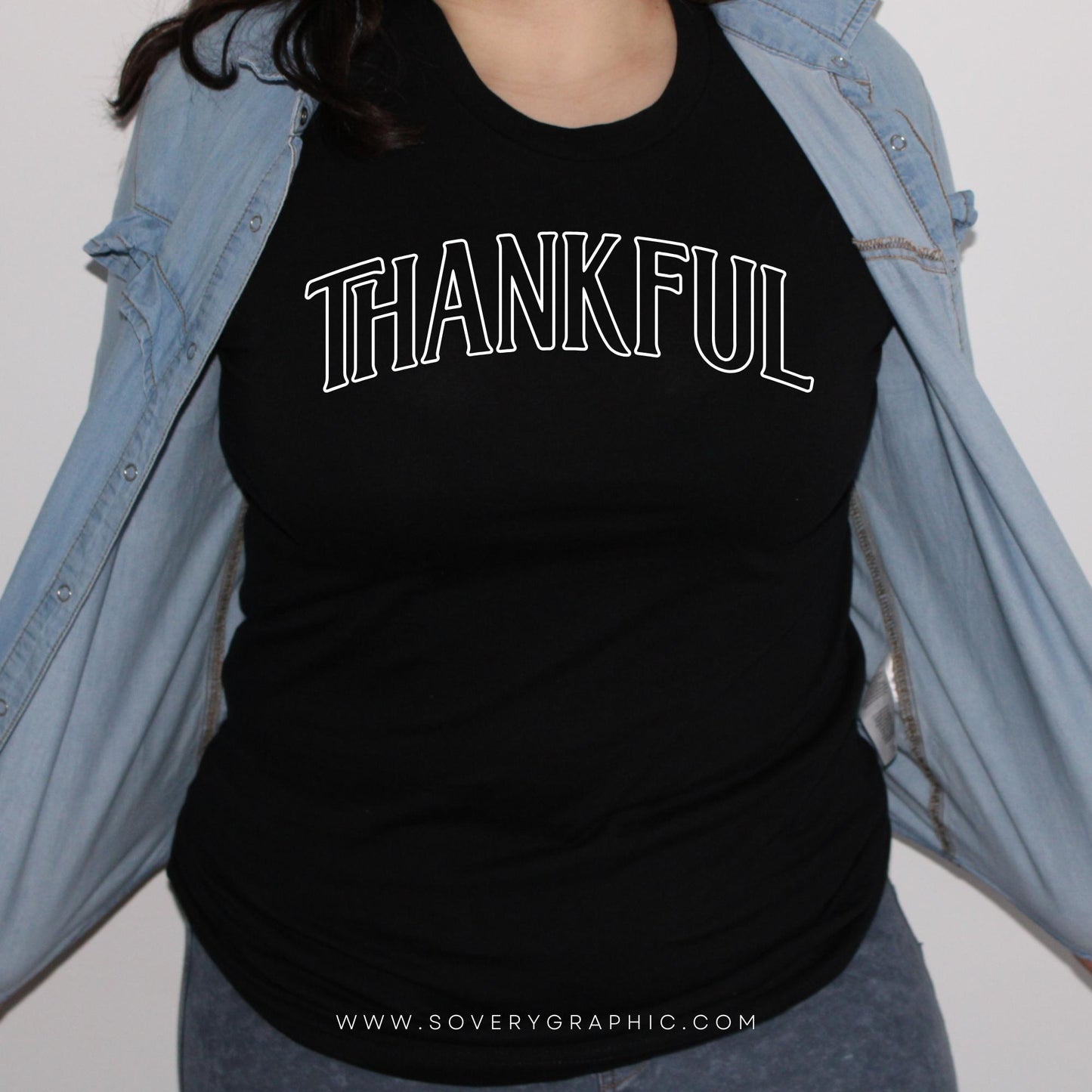 Woman wearing a black t-shirt with 'THANKFUL' text, light blue denim shirt, on a plain background