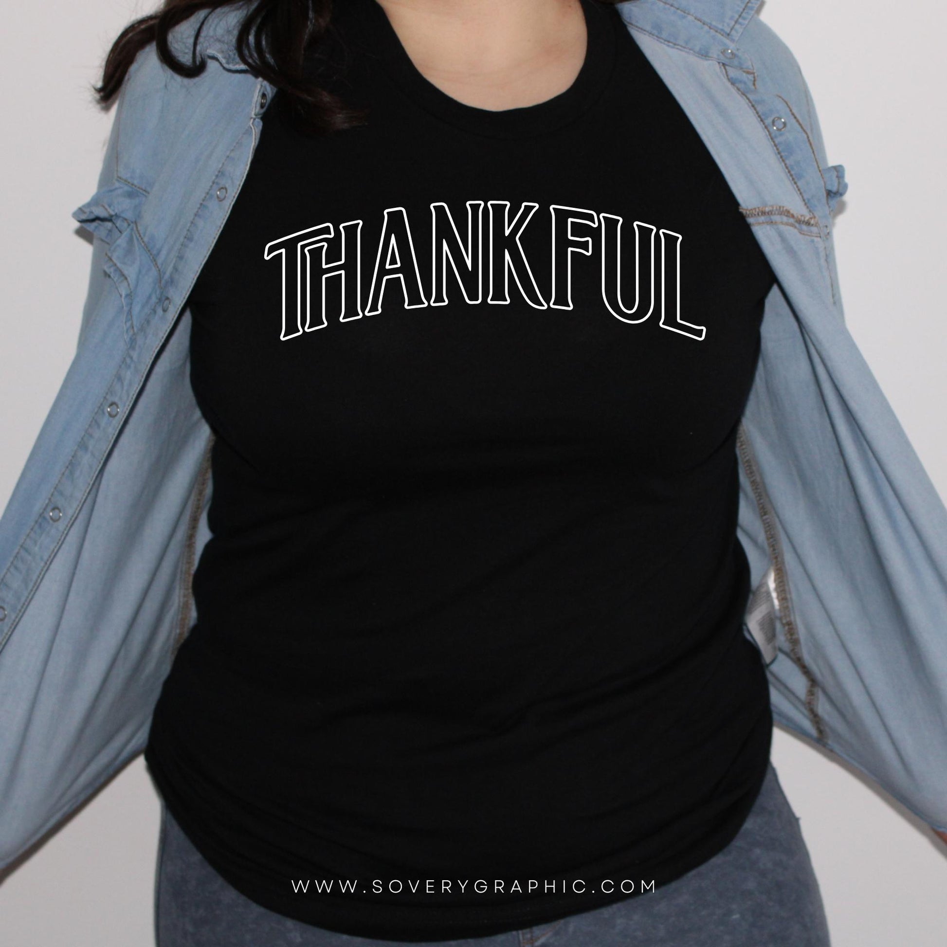Woman wearing a black t-shirt with 'THANKFUL' text, light blue denim shirt, on a plain background