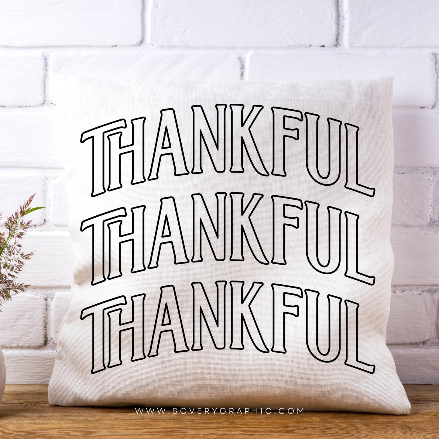 White pillow with 'THANKFUL' text on a white brick wall background