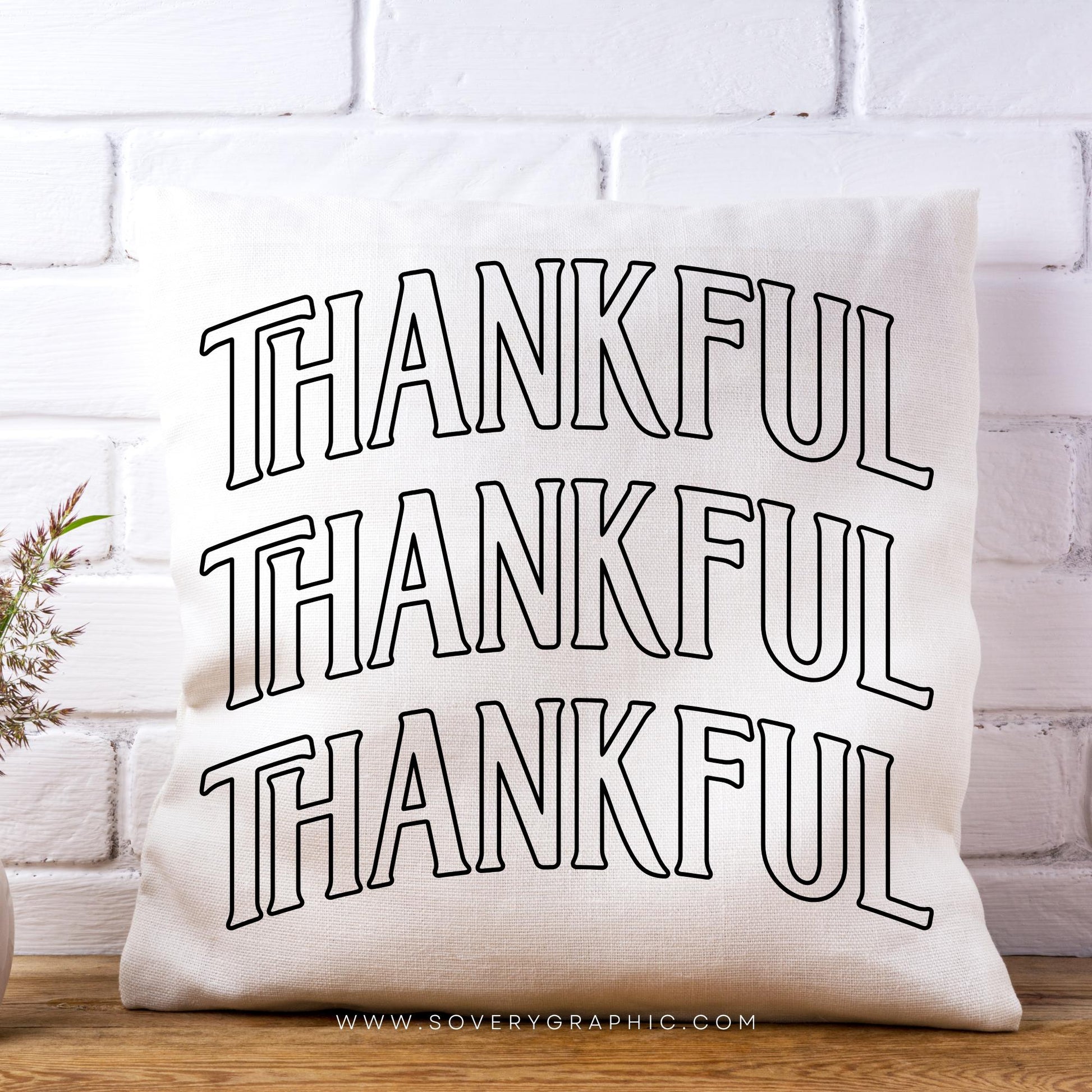 White pillow with 'THANKFUL' text on a white brick wall background